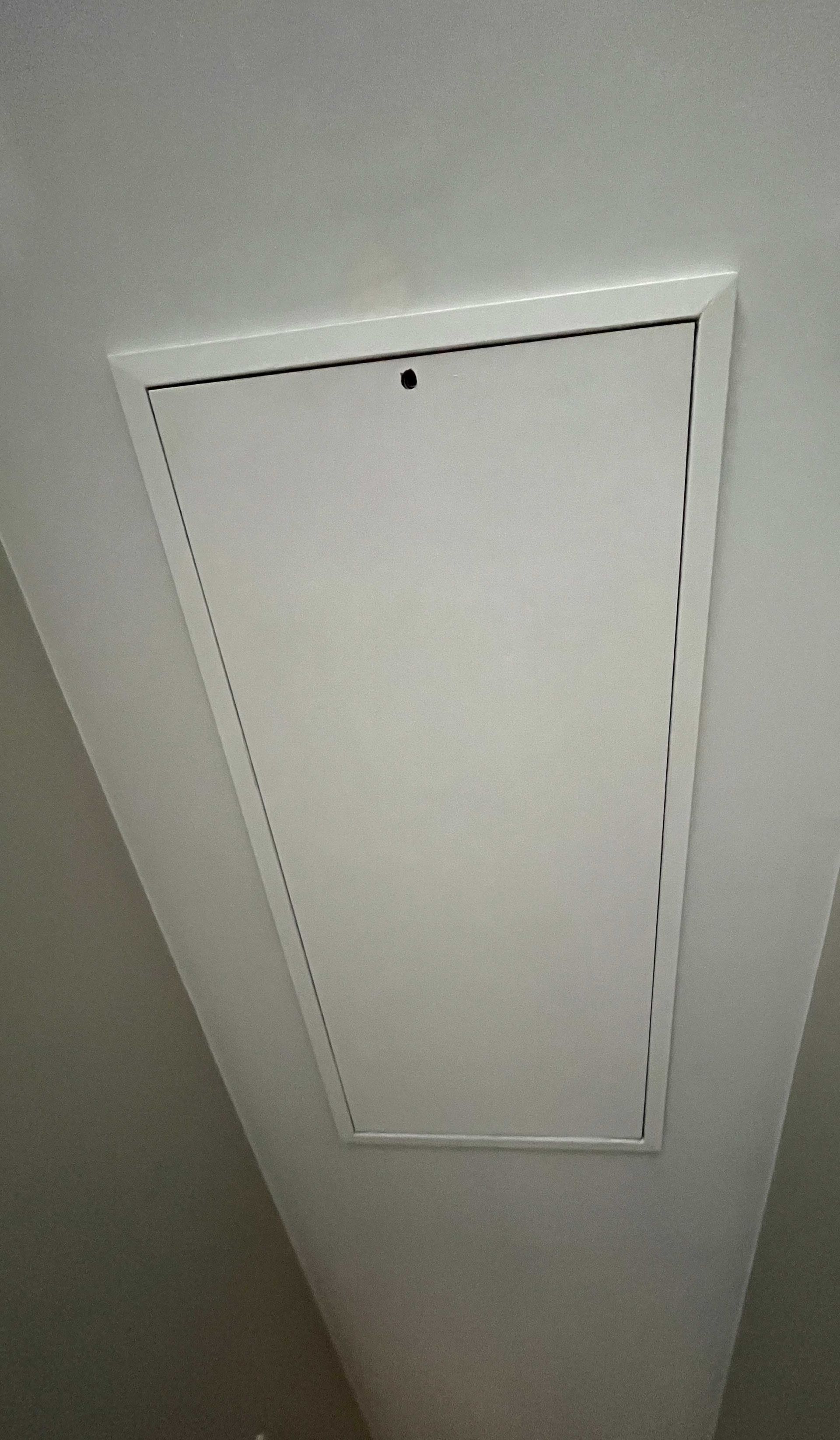 A white attic door is hanging from the ceiling of a room.