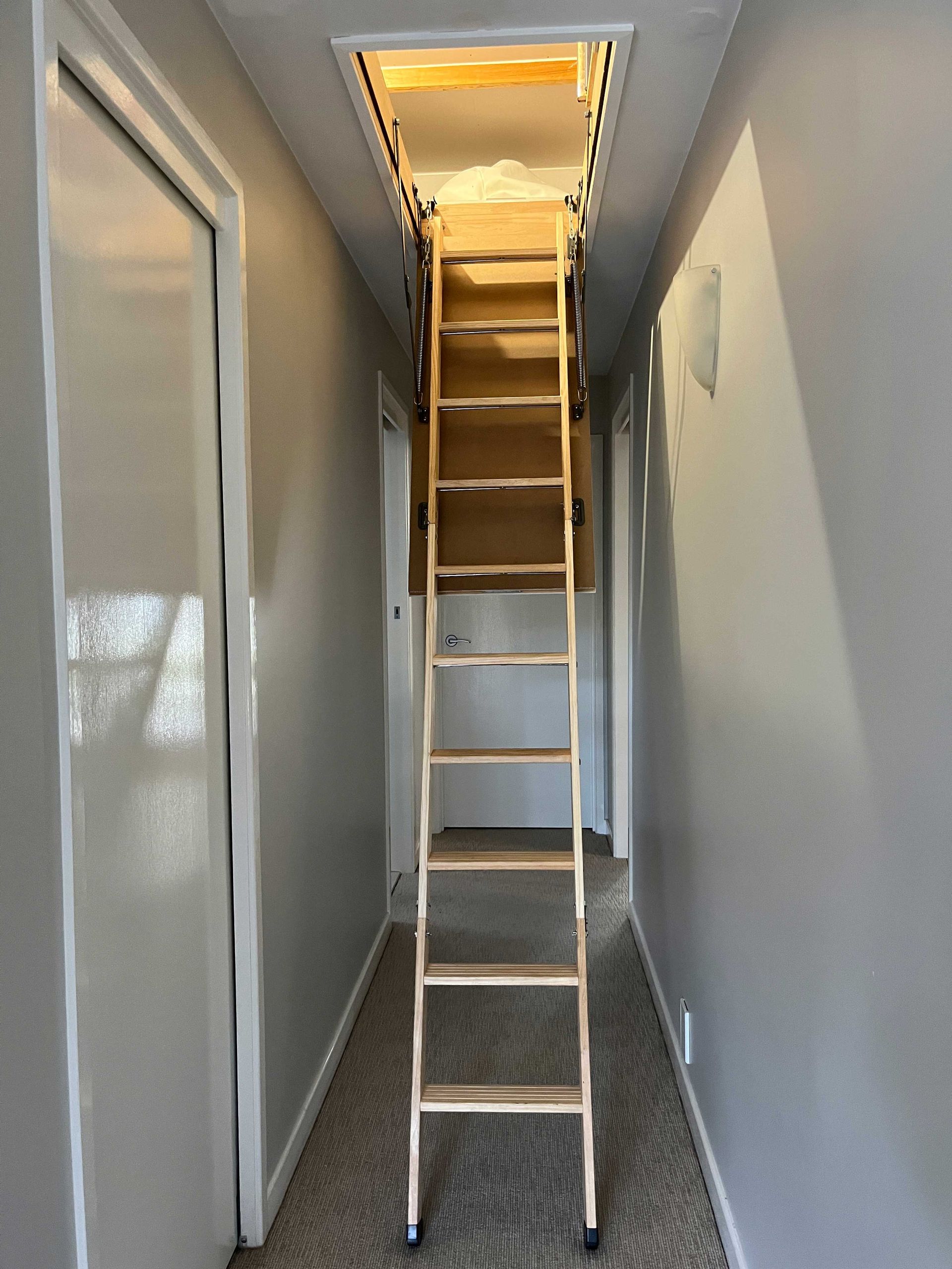 A wooden ladder is leading up to the attic in a hallway.