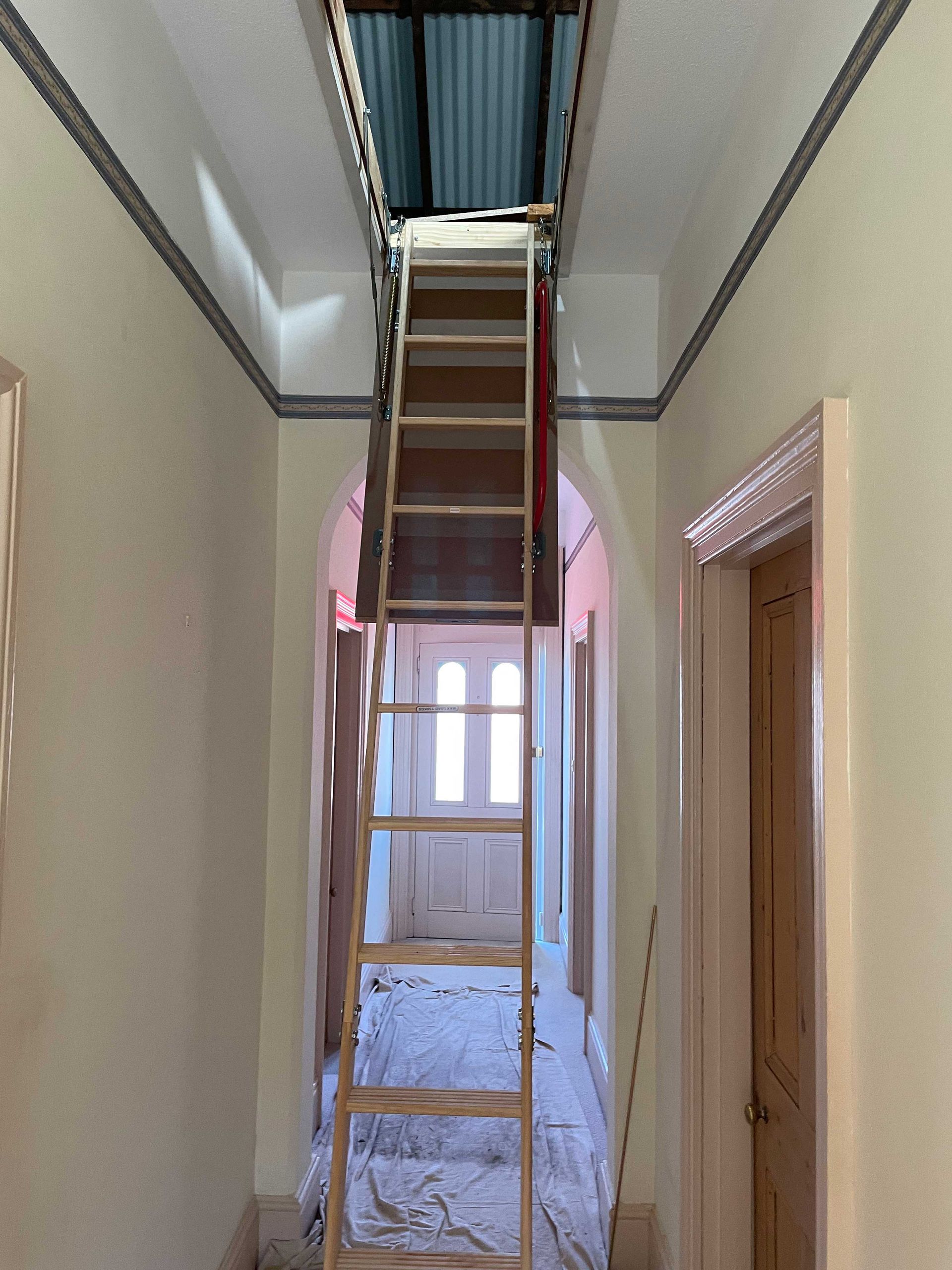 A wooden ladder is leading up to the attic in a hallway.