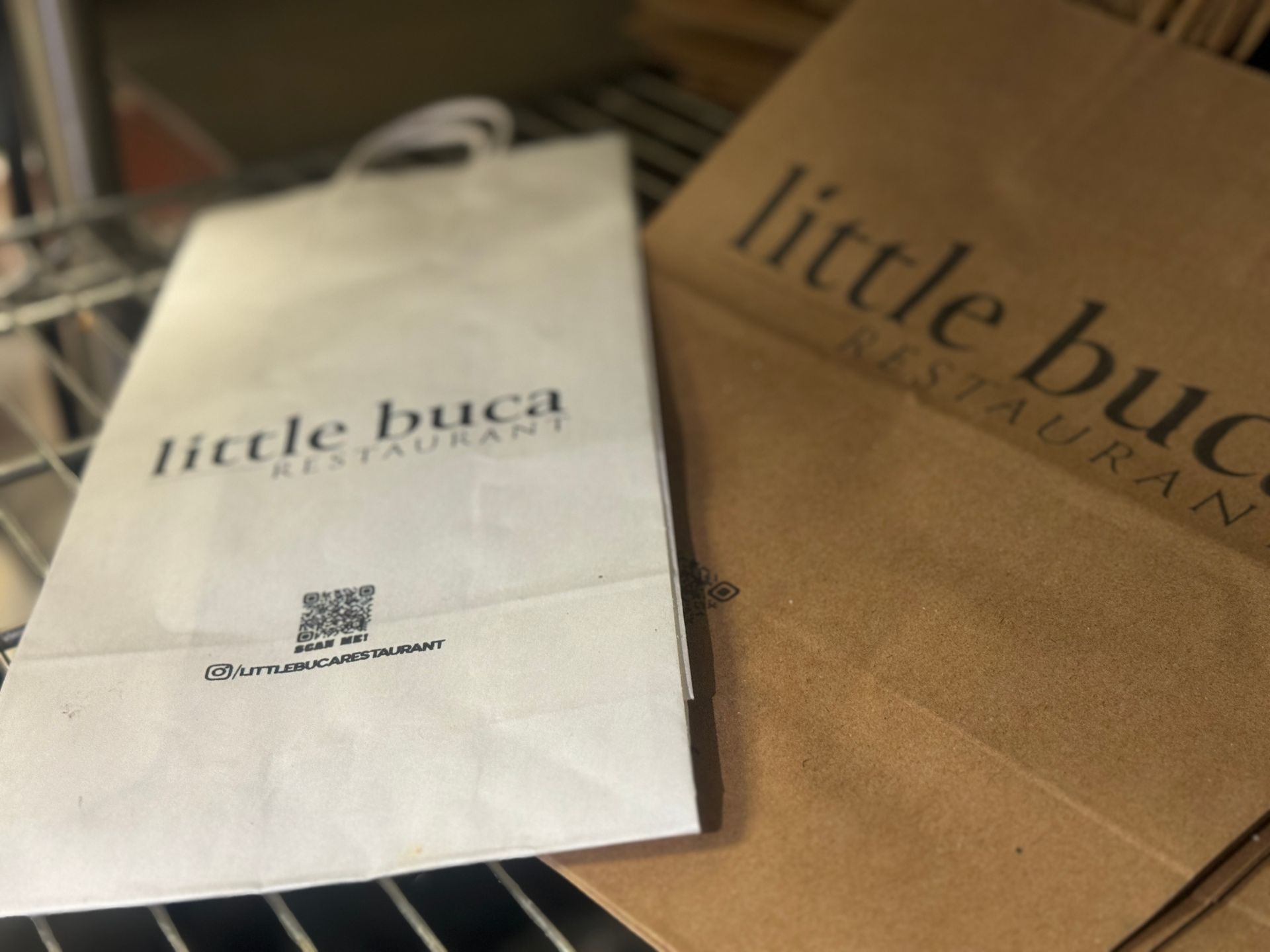 A little buca restaurant paper bag sits on a shelf
