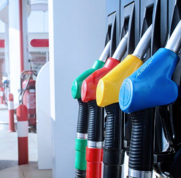 Kleurrijke brandstofpompmondstukken bij een benzinestation, met rode, gele en blauwe hendels op een rij.