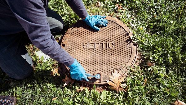 A man is kneeling down to open a septic tank cover.