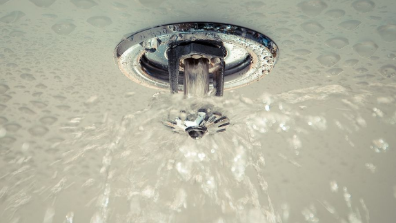 Water spraying from a sprinkler head on a white ceiling.