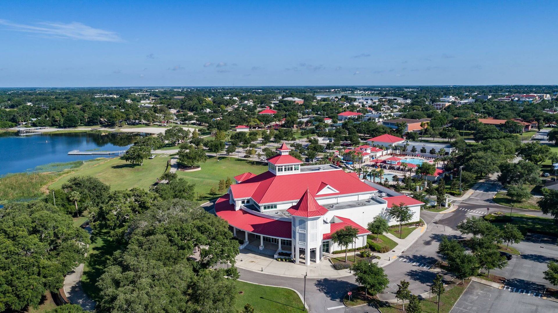 An aerial view of a large white building with a red roof surrounded by trees and a lake.