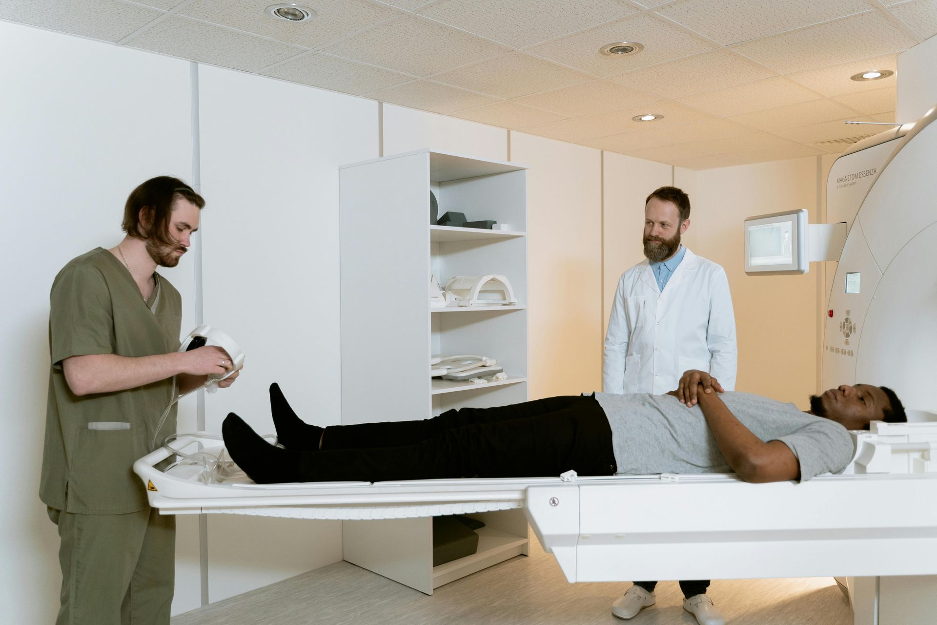 Man lying on examination table, two medical professionals attending him in a medical setting.