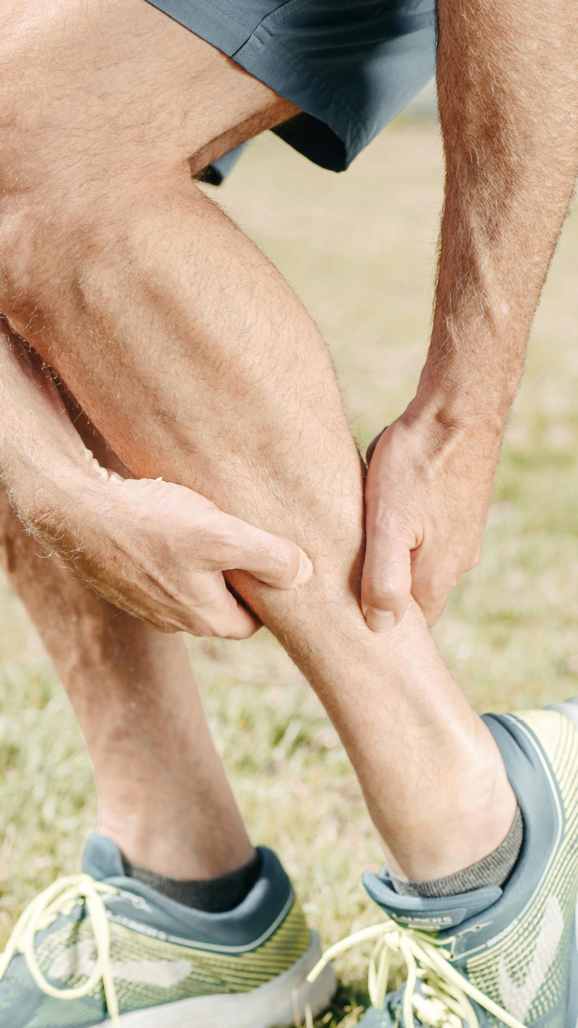 A person in running shoes holds their lower leg, gripping their calf in pain.