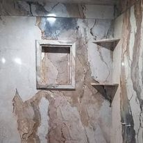 A bathroom with marble walls and shelves and a shower stall.