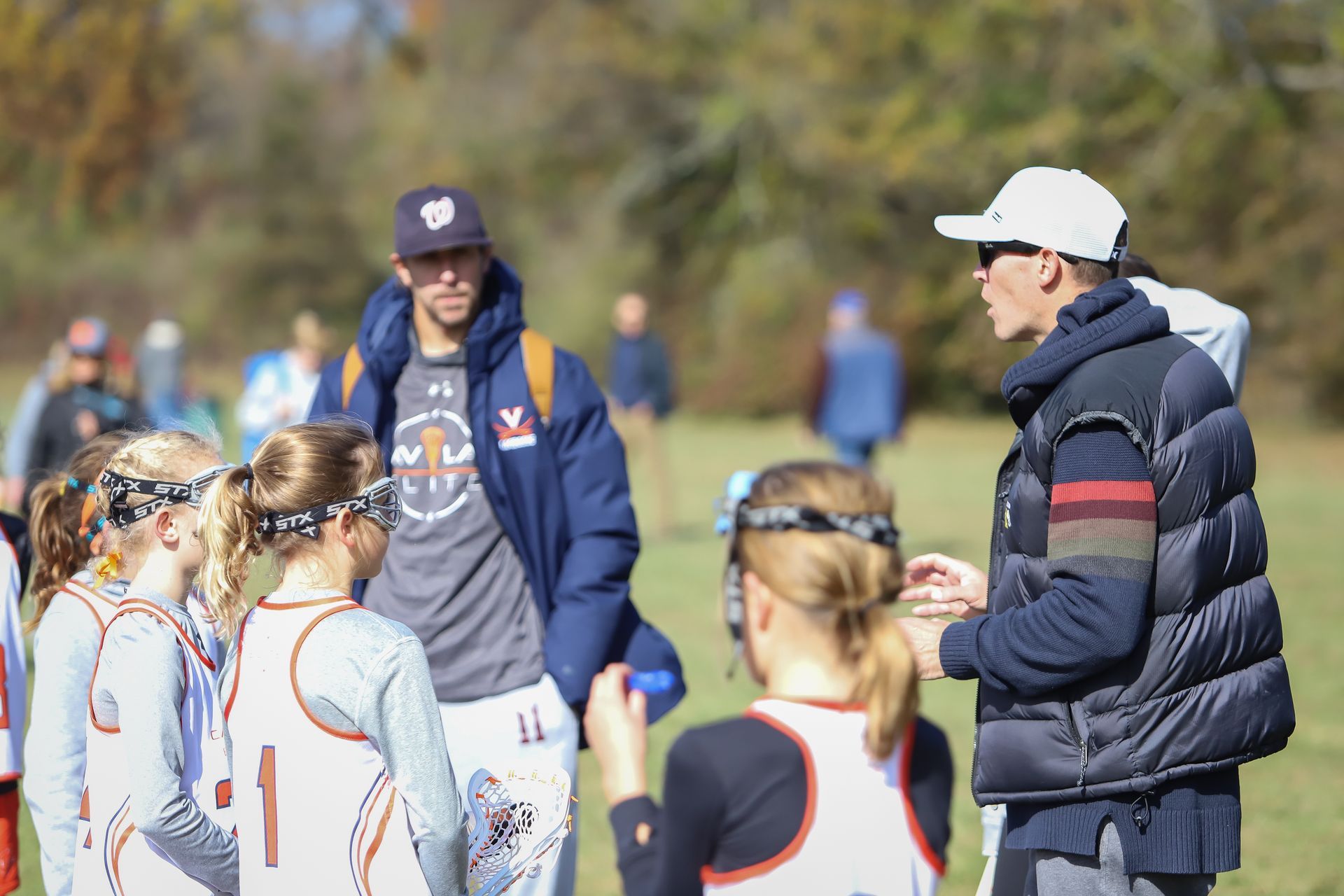 Group of younger girl lacrosse players standing on sideline with coach