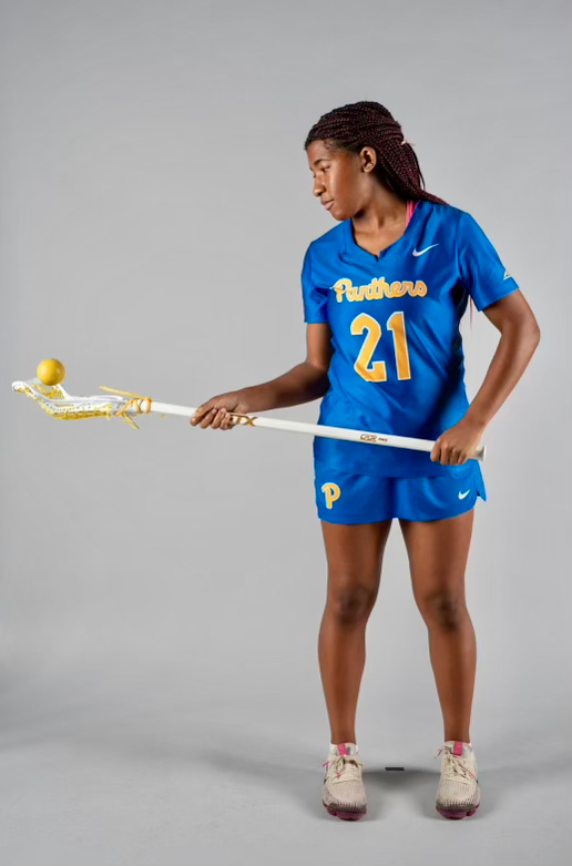 A woman in a blue shirt with the number 21 on it is holding a lacrosse stick
