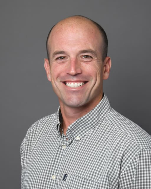 Headshot of CAV Lax Elite boys coach in white checkered shirt, smiling