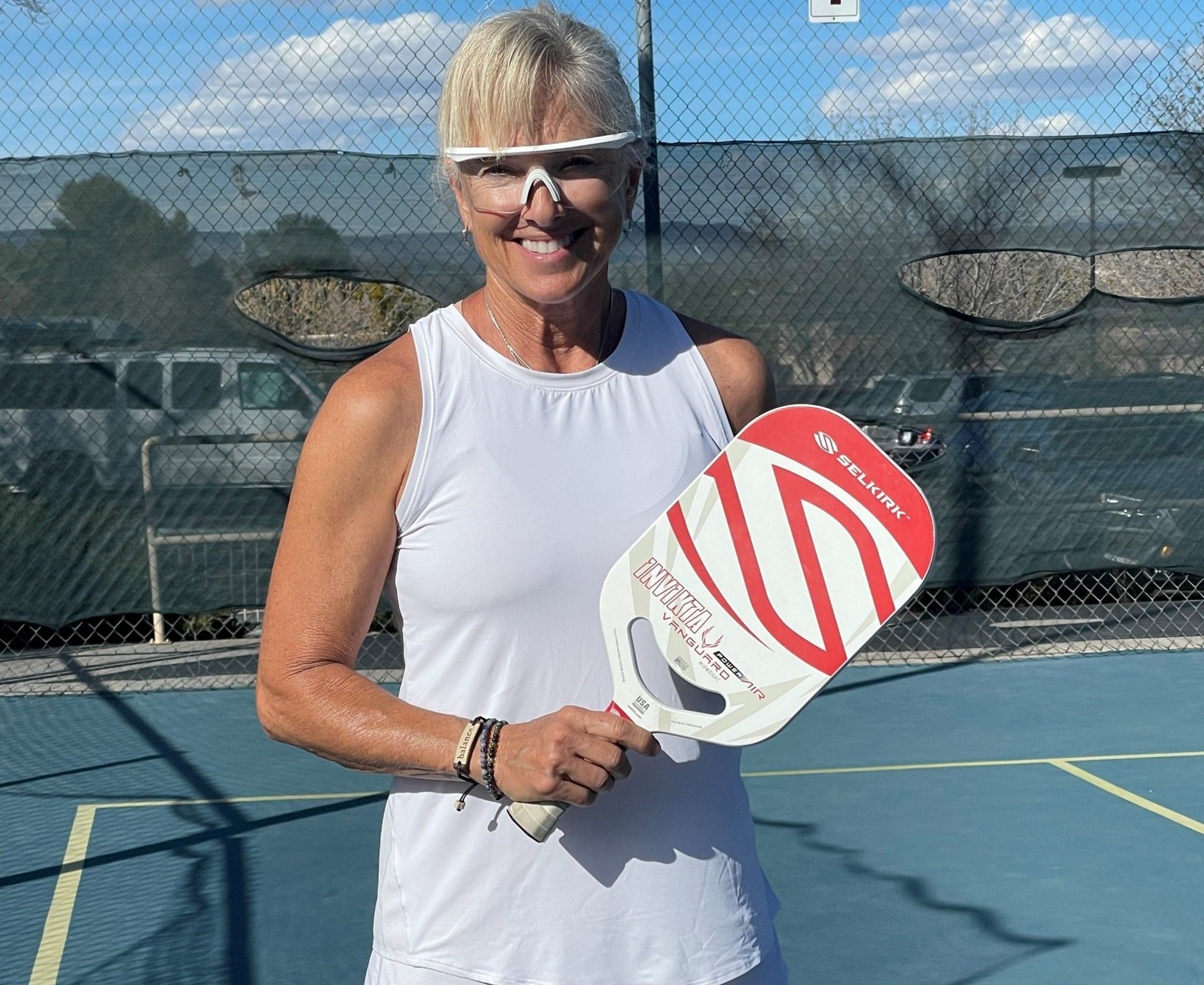 A woman is holding a red and white paddle on a tennis court.