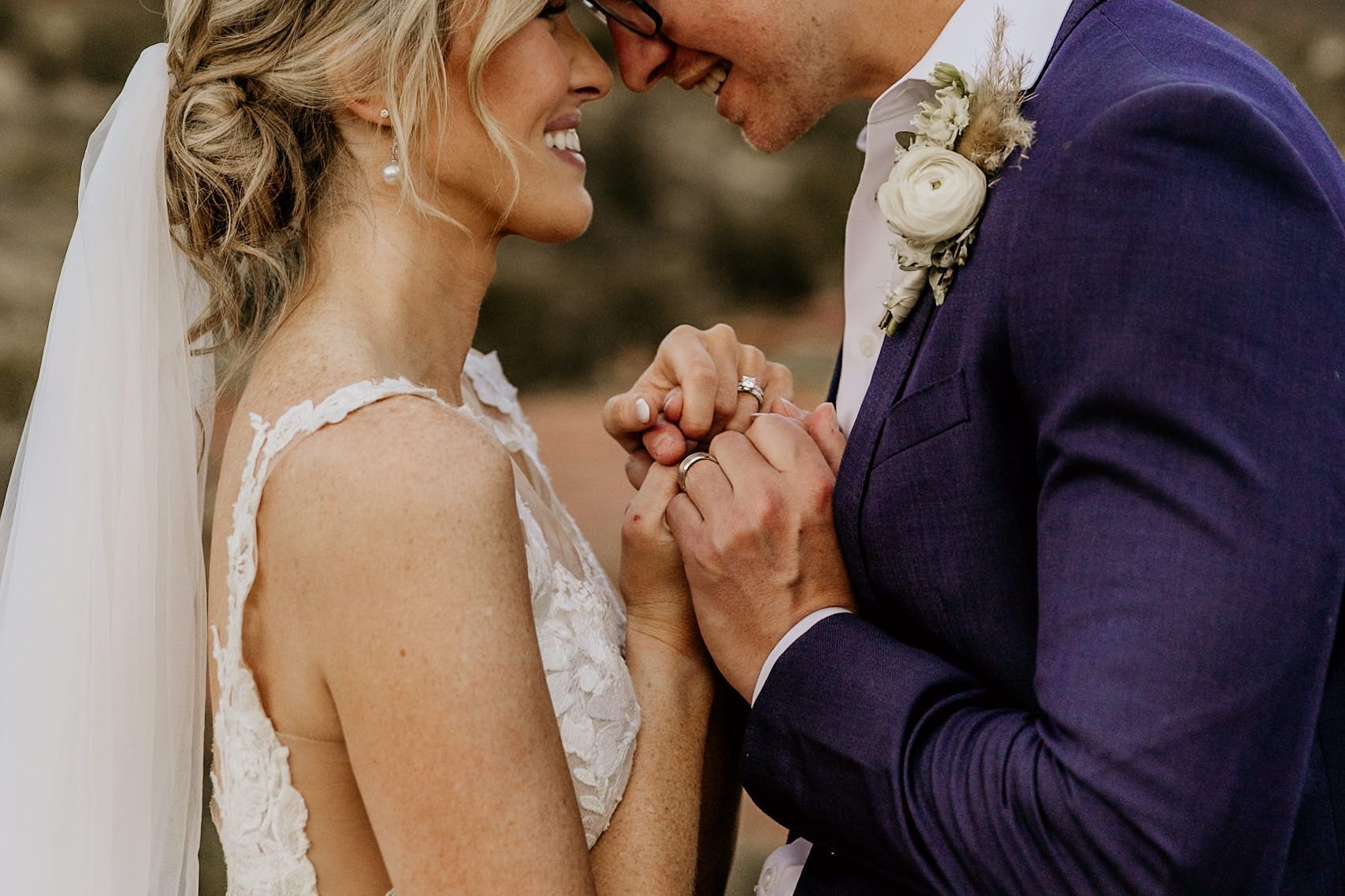 A bride and groom are holding hands and smiling at each other.