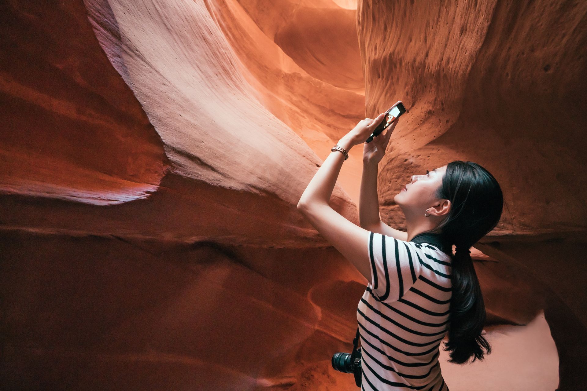 A woman is taking a picture of a canyon with a cell phone.