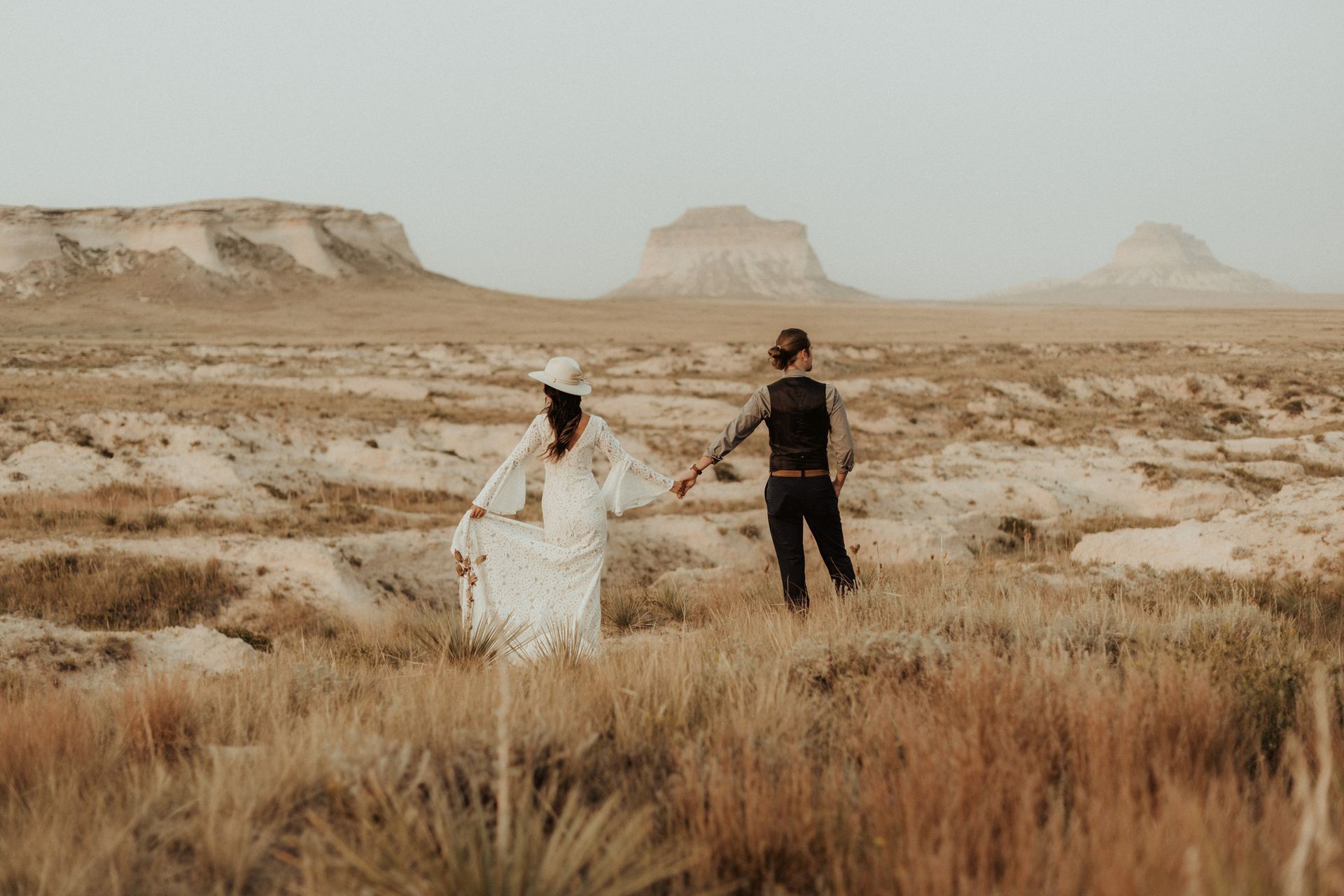 A bride and groom are holding hands in the desert.