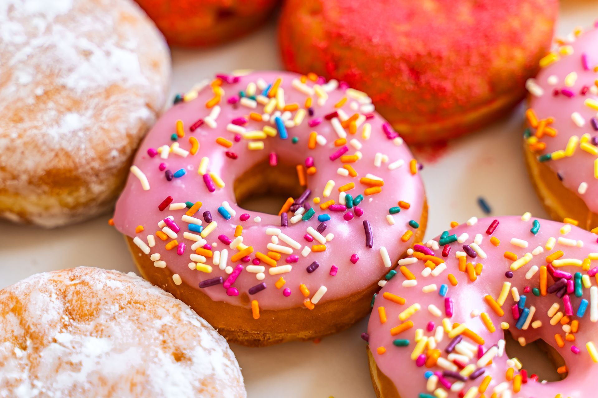 A variety of donuts with pink frosting and sprinkles on a white plate.