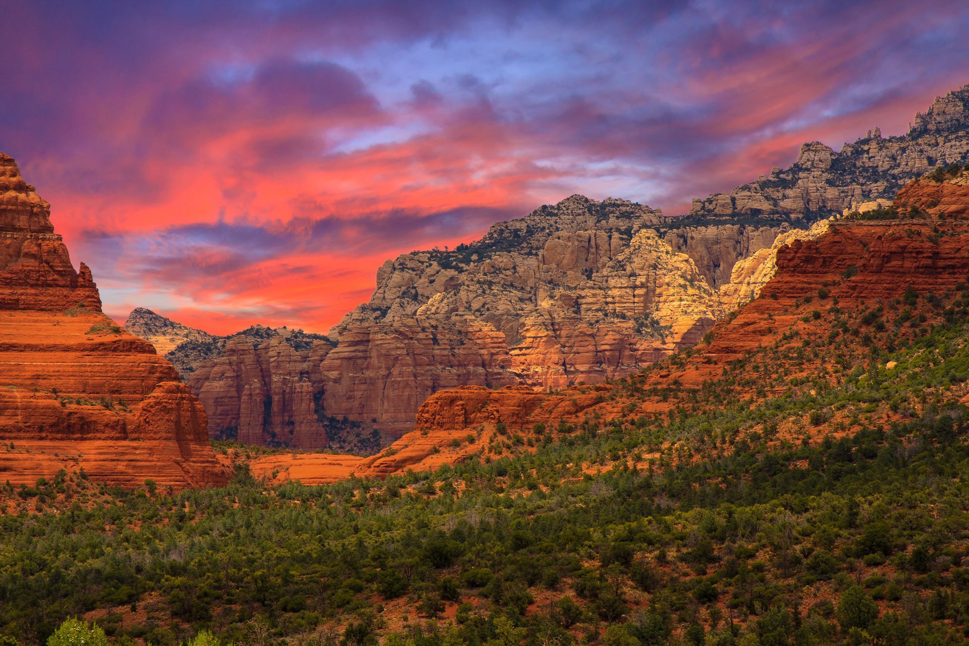 A sunset over a canyon with red rocks and trees