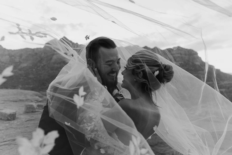 A black and white photo of a bride and groom covered in a veil.