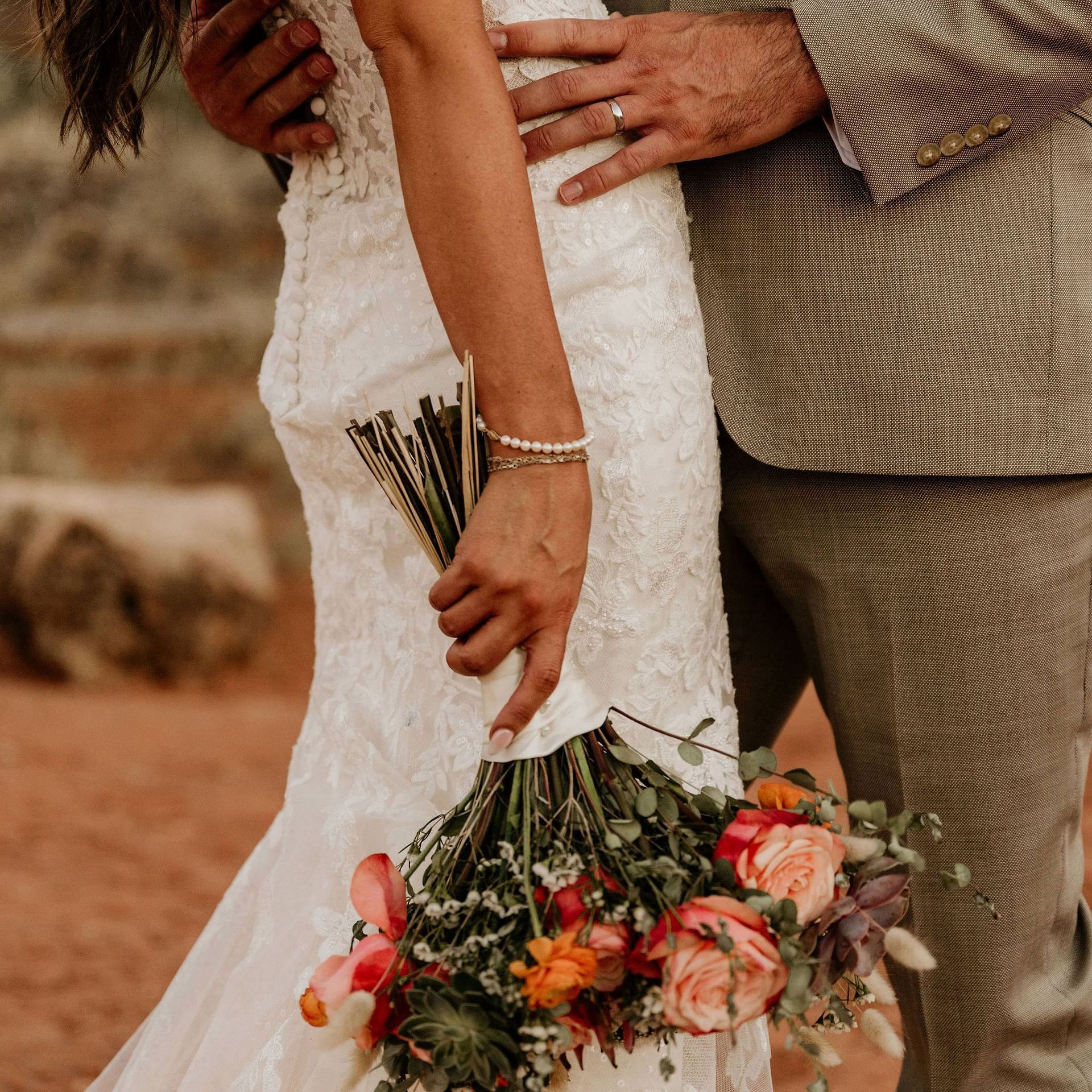 A bride and groom are posing for a picture while the bride is holding a bouquet of flowers.