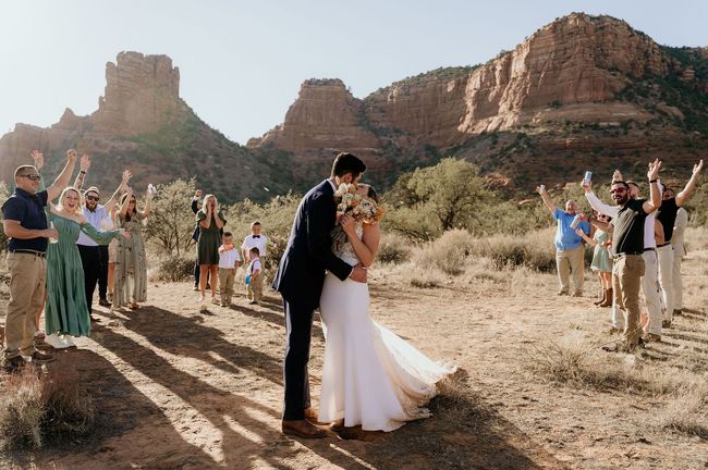A bride and groom kissing in front of a crowd of people at their wedding.