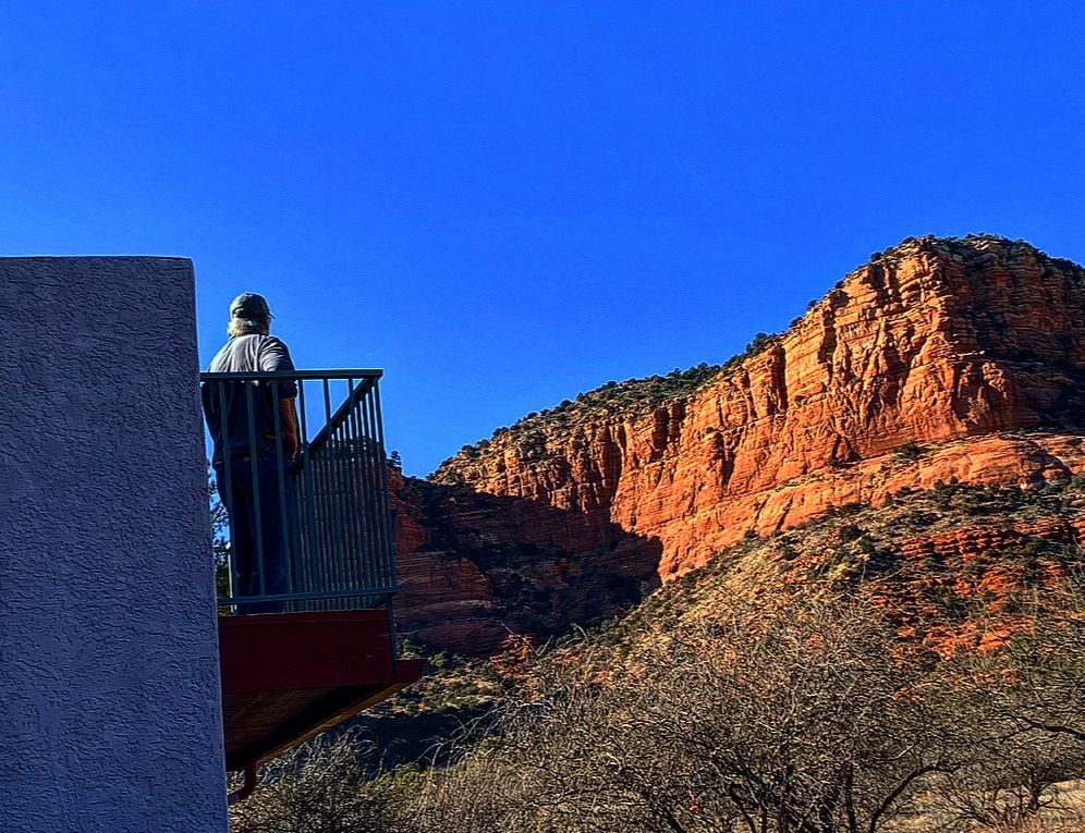 A man is standing on a balcony overlooking a mountain.