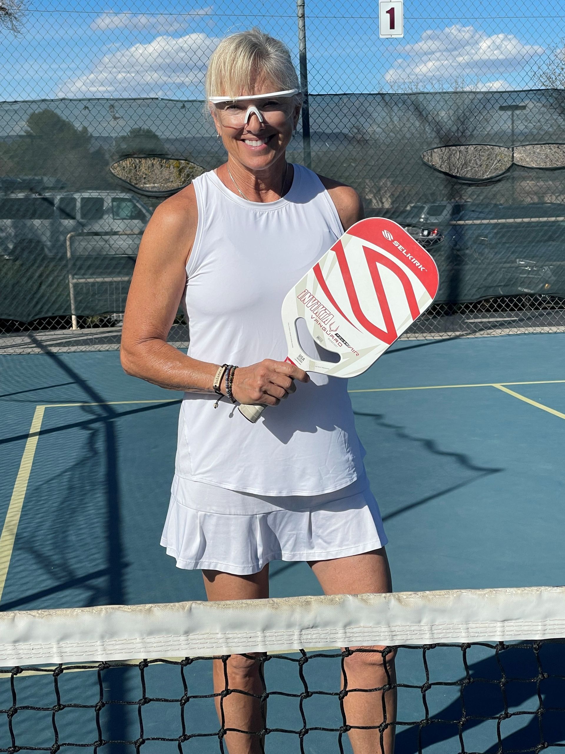 A woman is holding a red and white paddle on a tennis court.