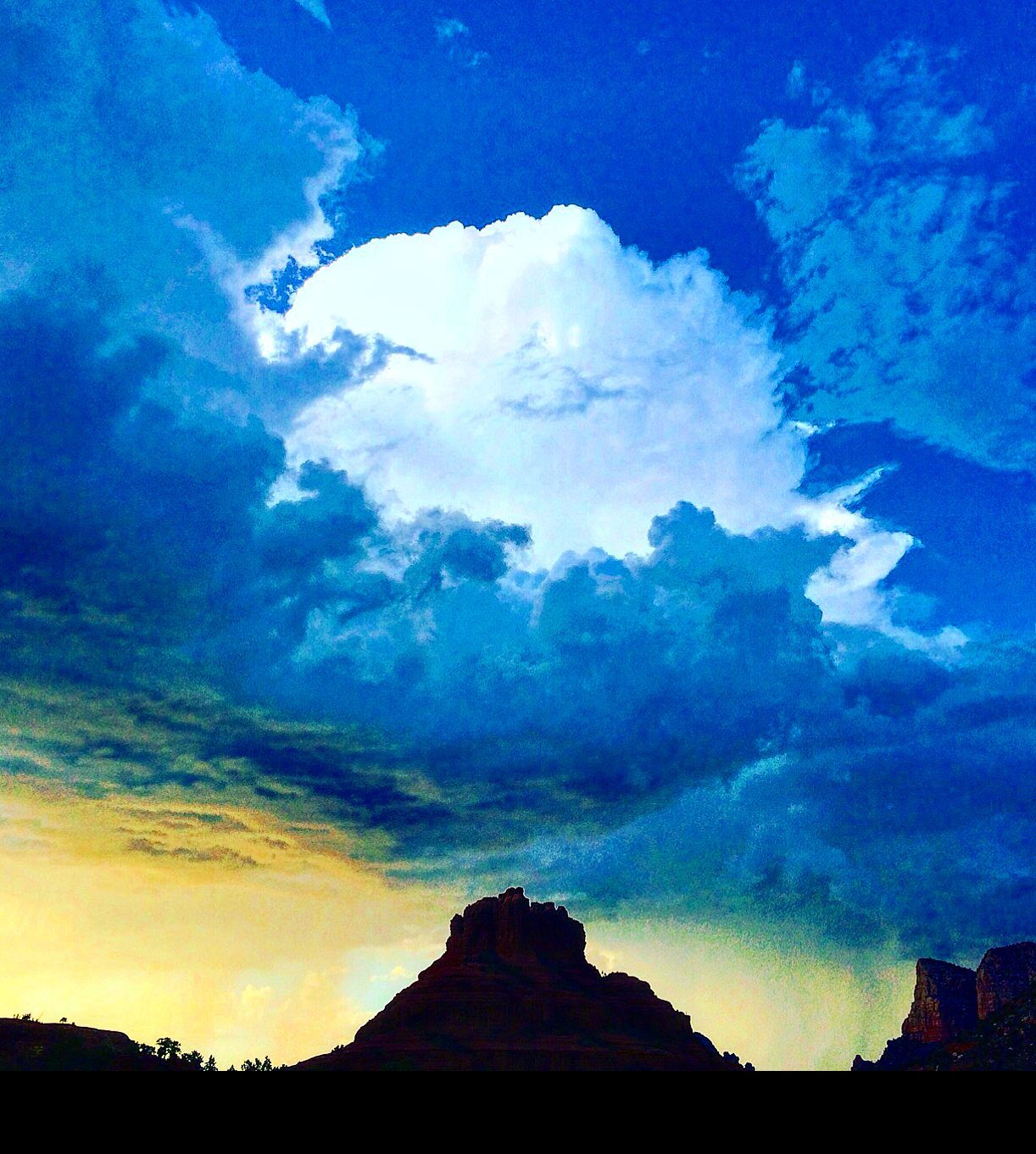 A mountain silhouetted against a blue sky with clouds