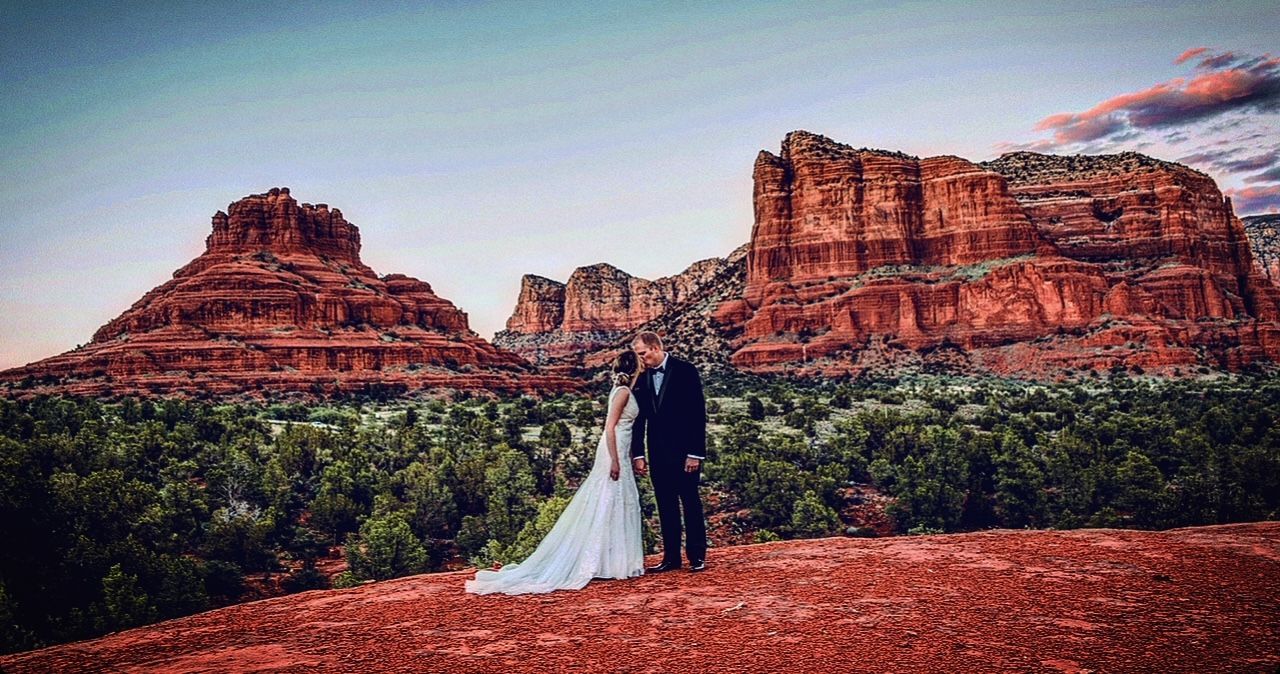 A bride and groom are posing for a picture in front of a mountain range.