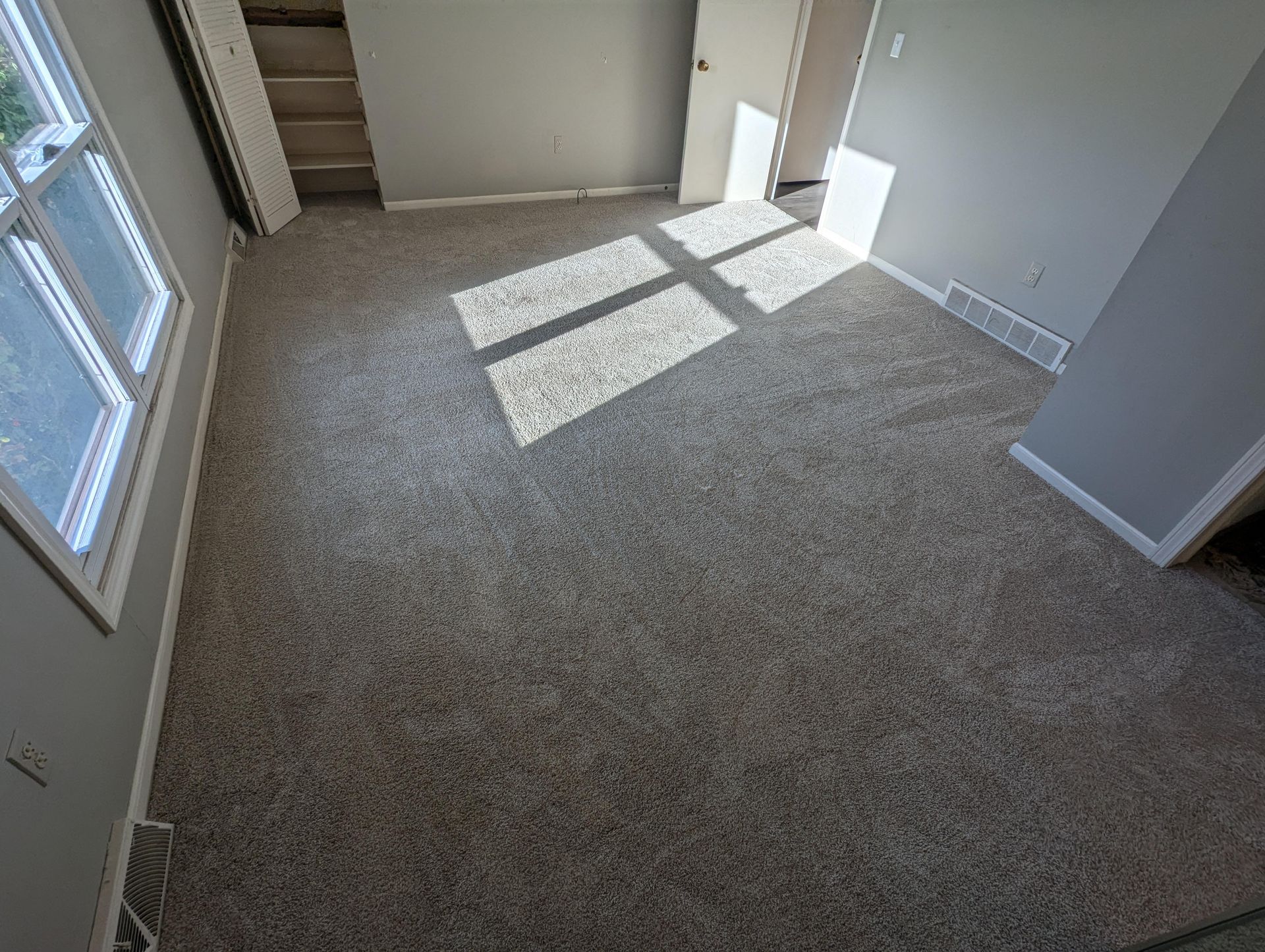 A bedroom with a carpeted floor and a window.