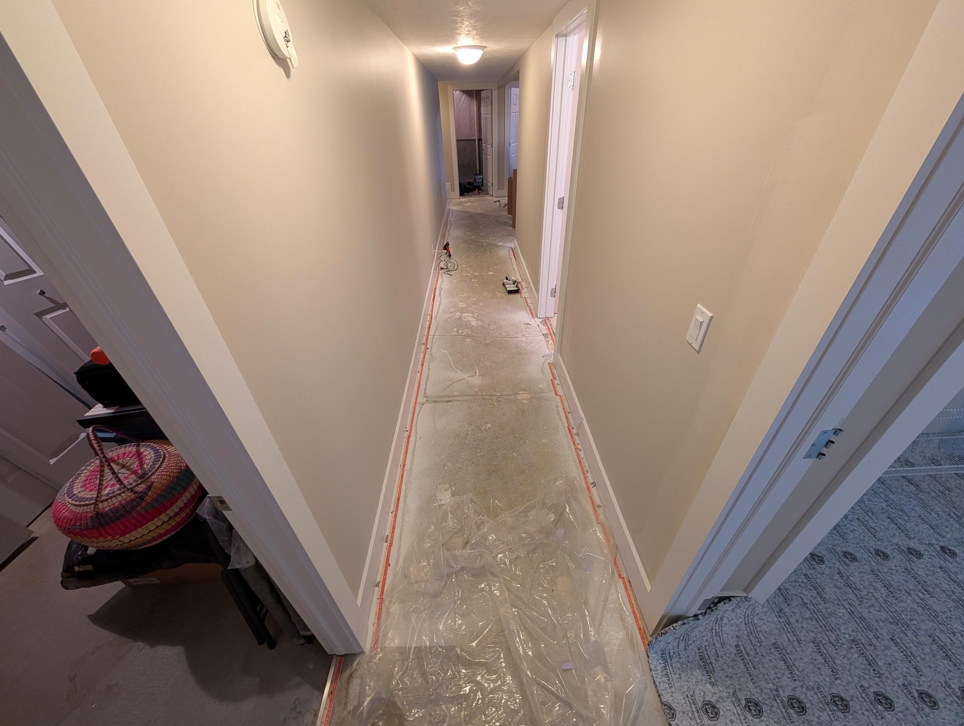 A long hallway with plastic covering the floor is being painted.