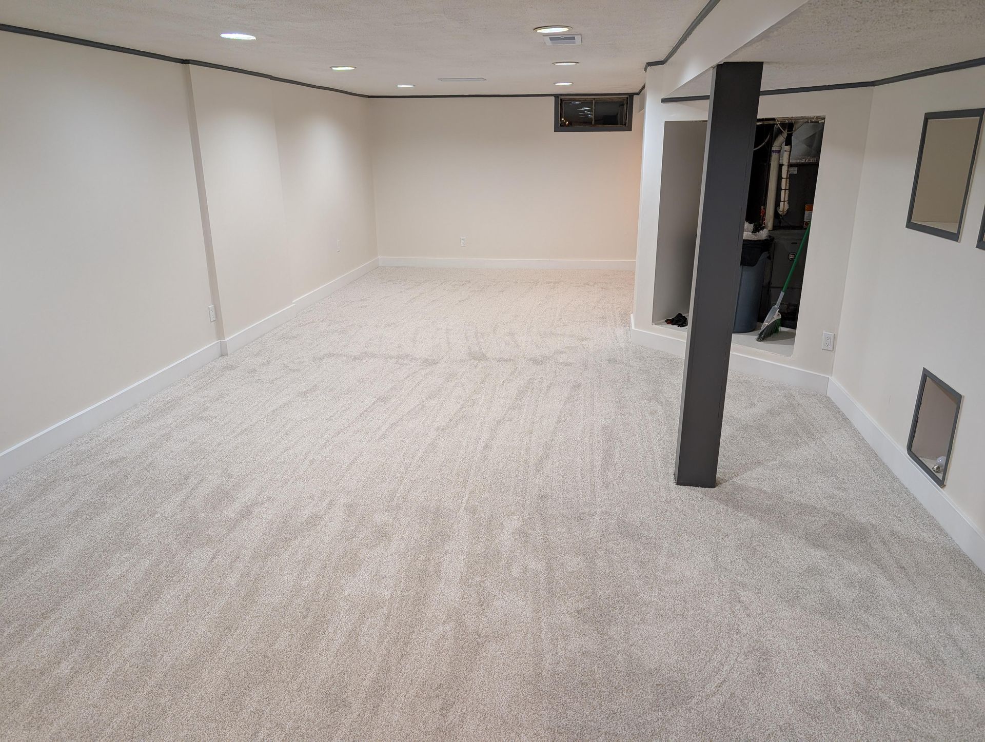 An empty basement with a carpeted floor and white walls.