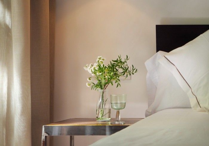 Un jarrón de flores reposa en una mesita de noche al lado de una cama.