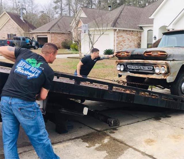 Two men pushing a truck on a tow truck that says brothers towing