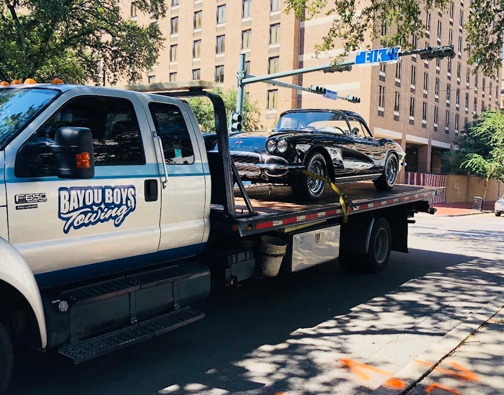 A tow truck is towing a black car on the back of it.