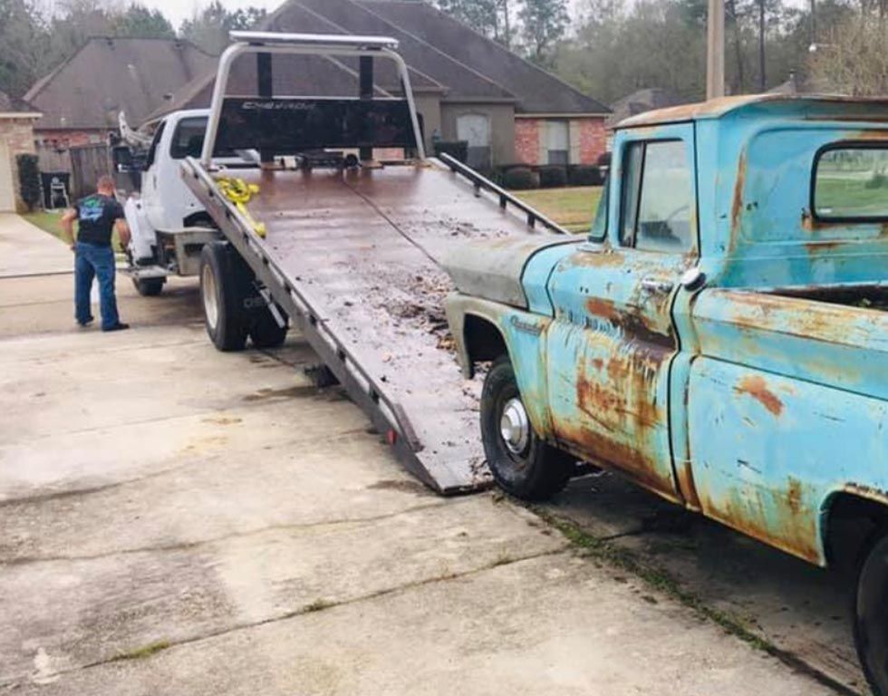 A man is standing next to a tow truck that is towing a blue truck.