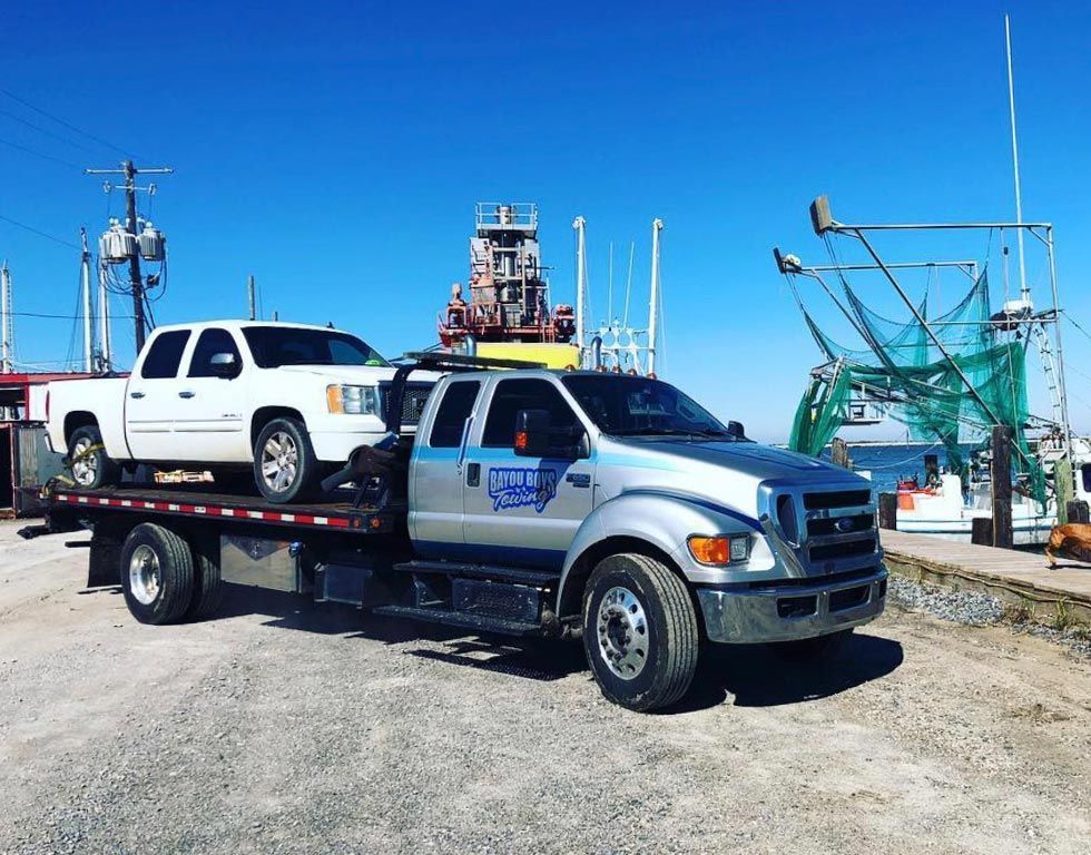 A tow truck is carrying two trucks on its flatbed.