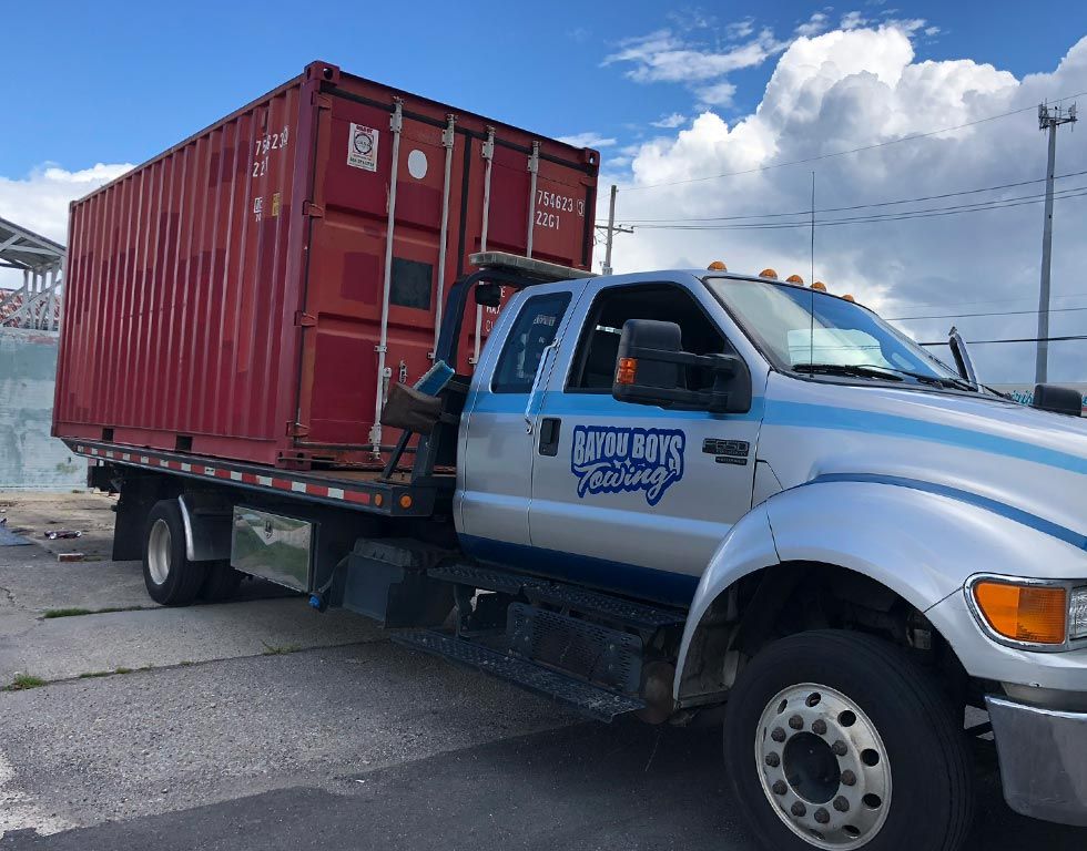 A tow truck is carrying a red shipping container.