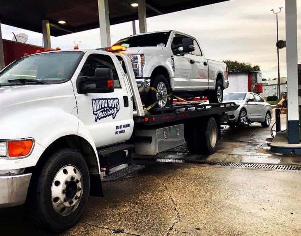 A tow truck is carrying a truck on the back of it.