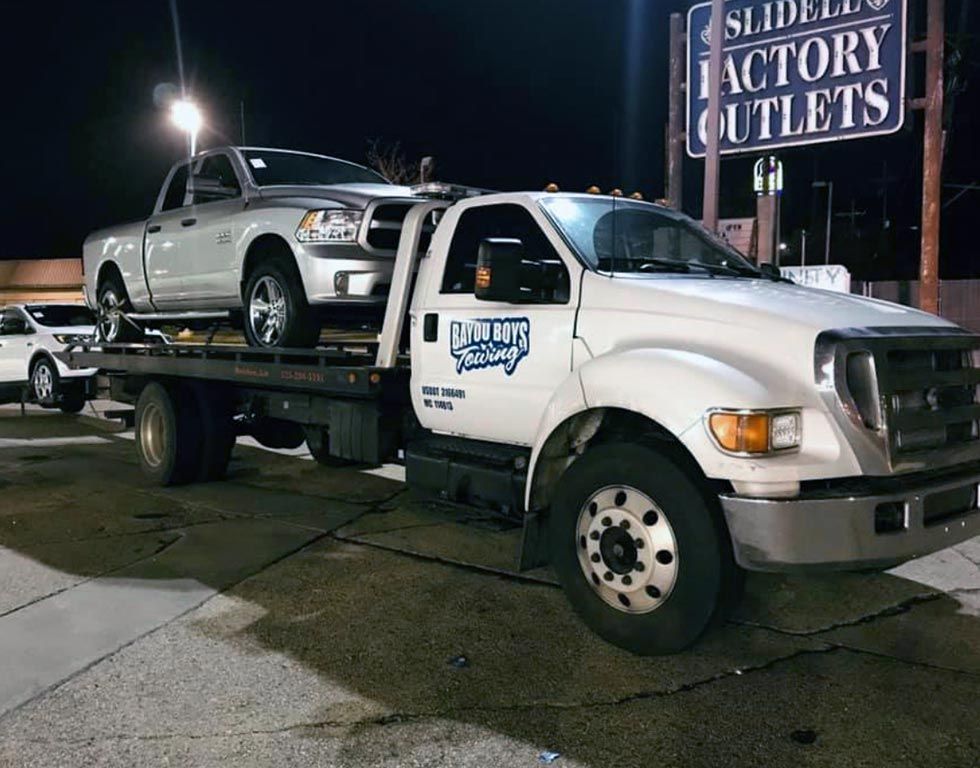 A tow truck with two cars on the back is parked in front of a sign that says factory outlets.