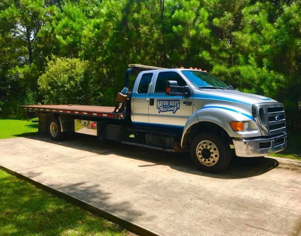 A tow truck with a flat bed is parked on the side of the road.