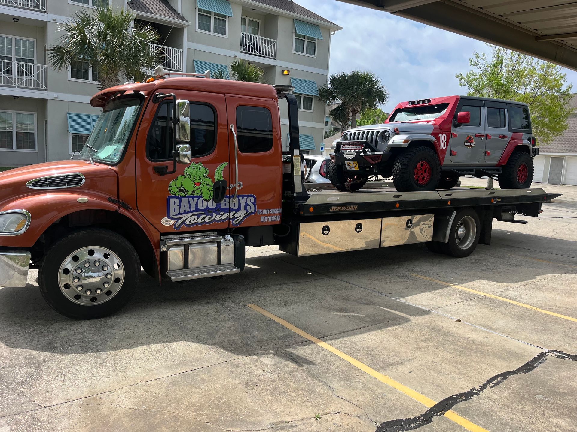 A tow truck with a jeep on the back is parked in a parking lot.