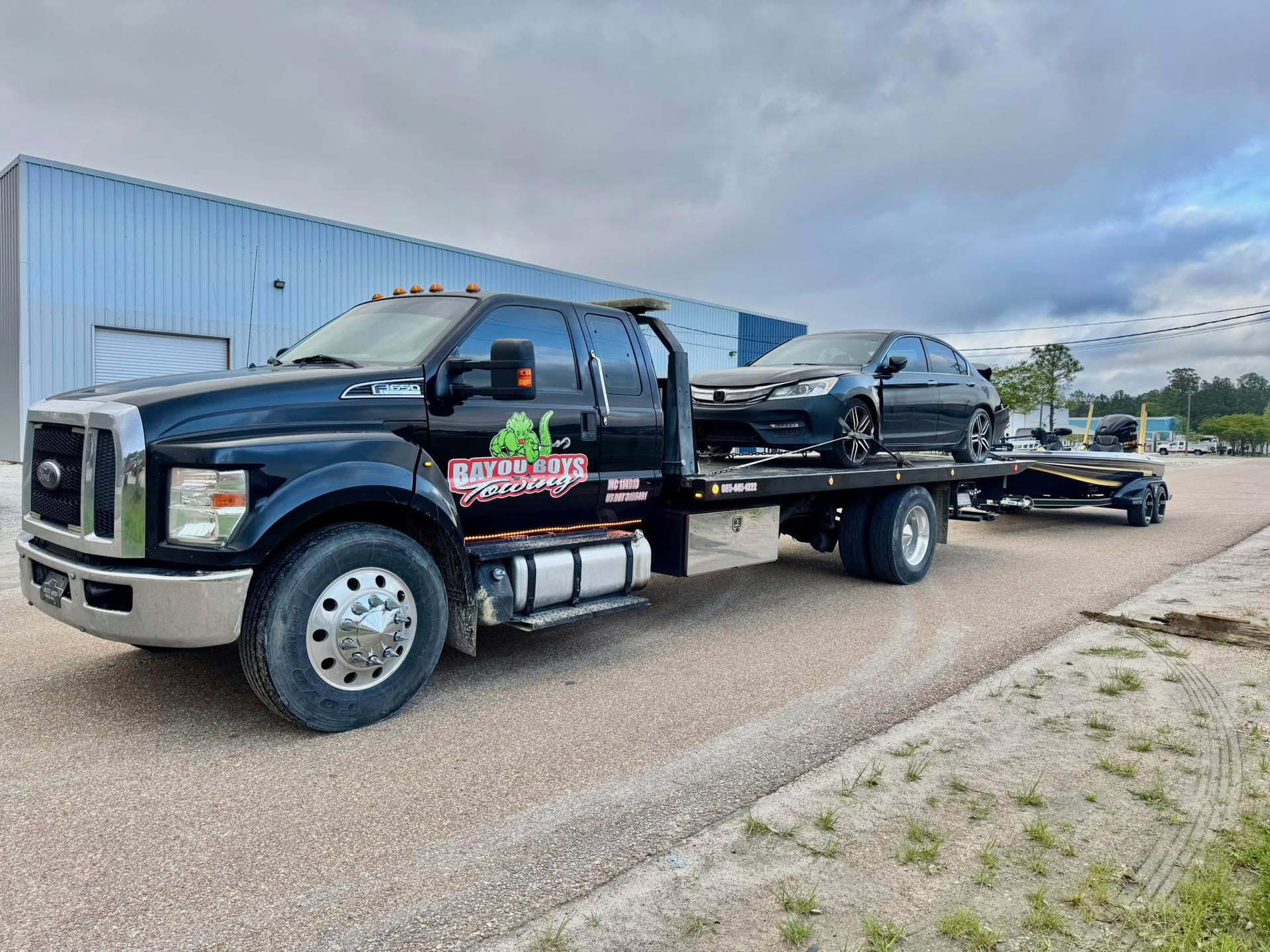 A black tow truck is towing a black car on a trailer.