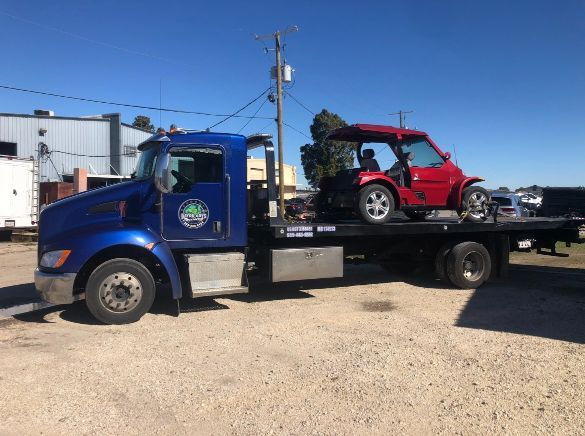A blue tow truck is towing a red golf cart.