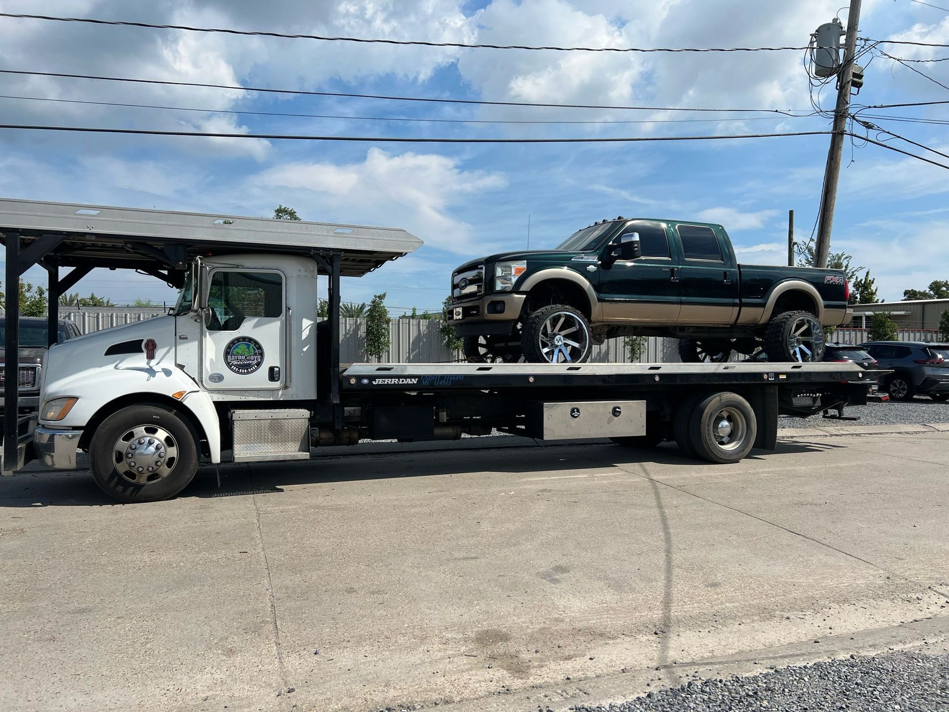 A tow truck is carrying a green truck on its flatbed.