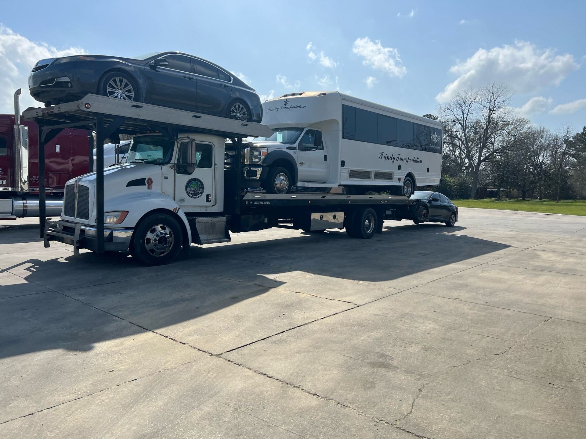 A tow truck is carrying a car and a bus.