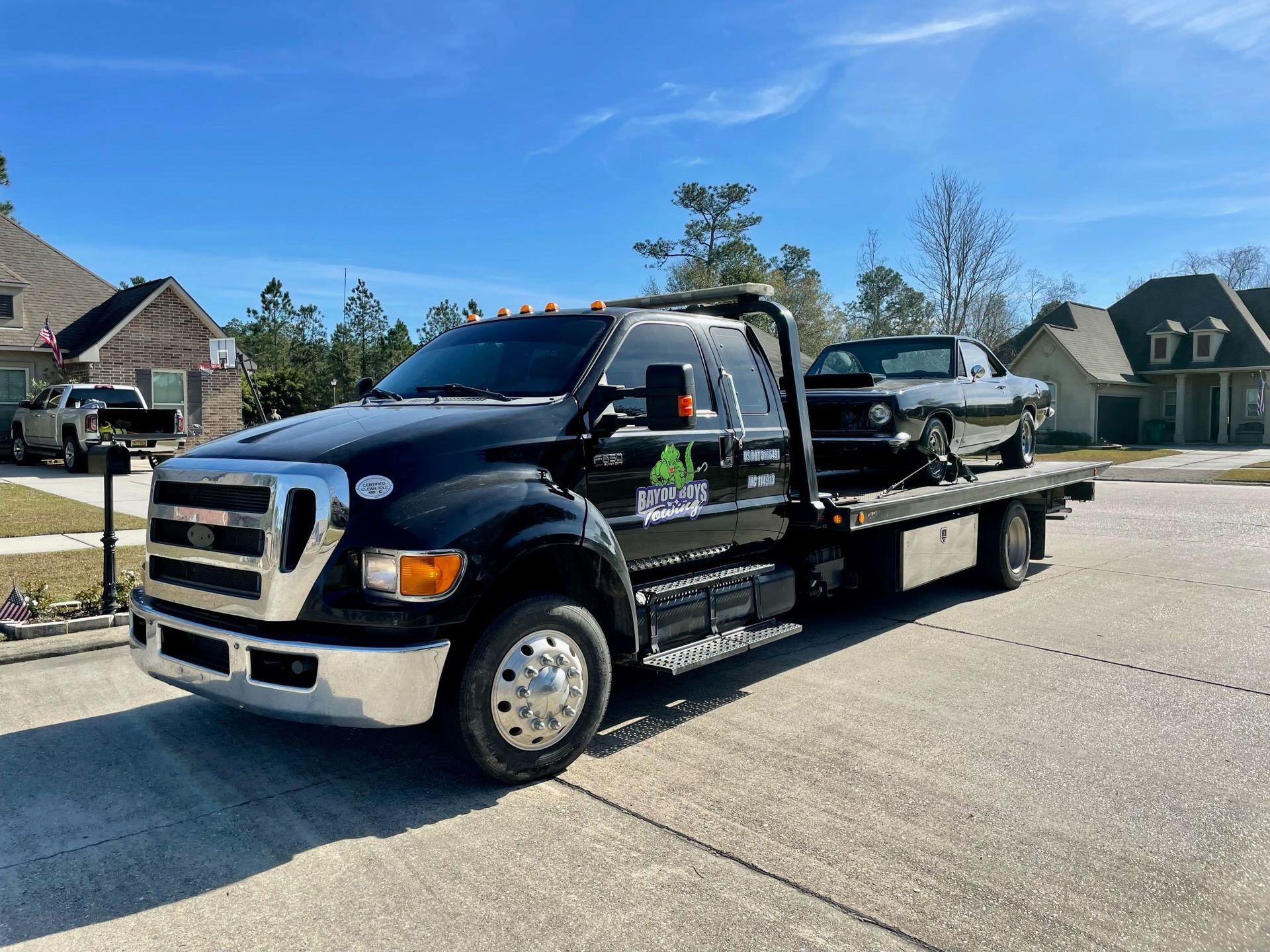 A black tow truck with a car on the back is parked on the side of the road.
