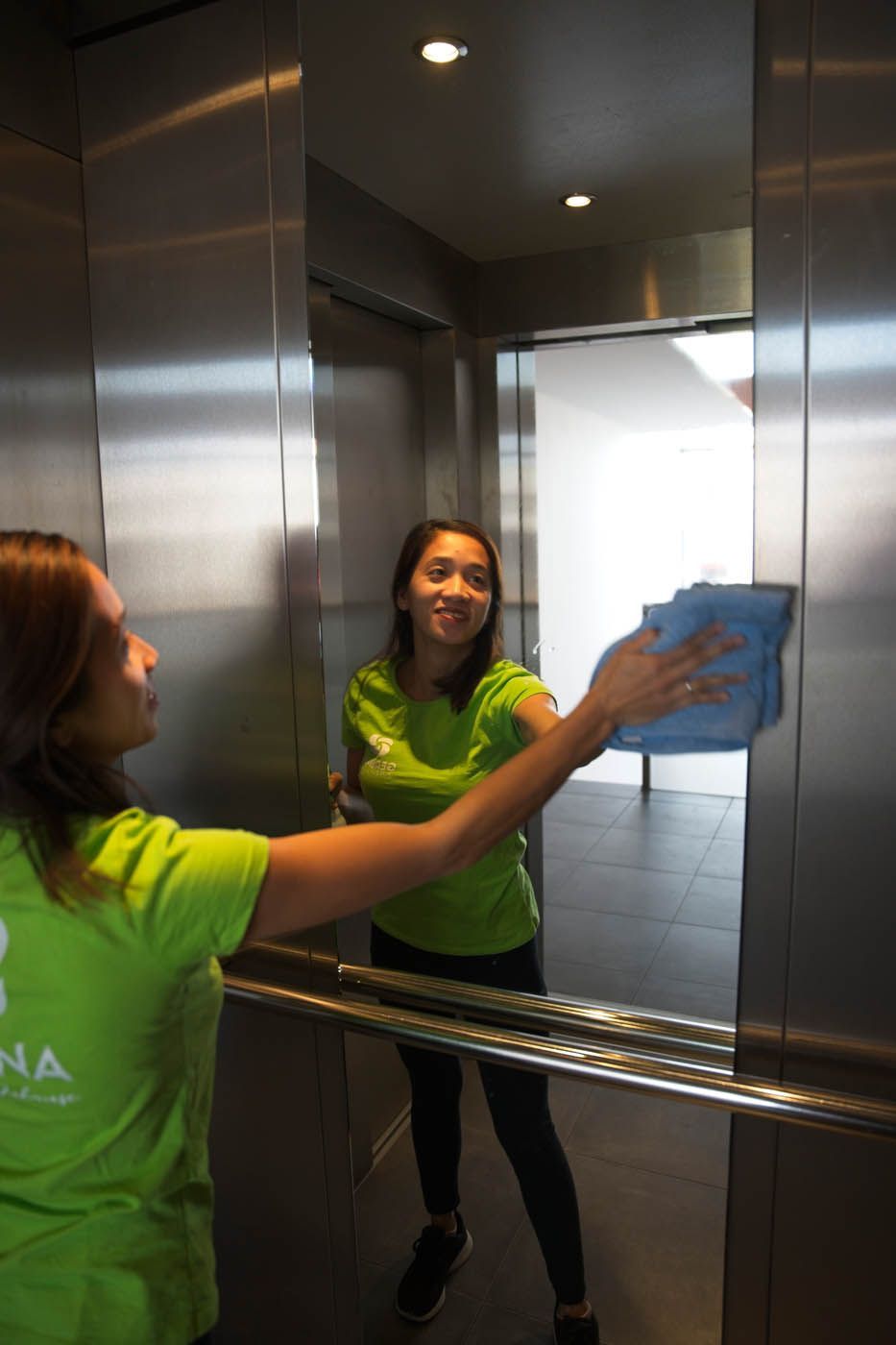 Frau in grünem Hemd wischt Aufzugspiegel mit blauem Tuch ab.