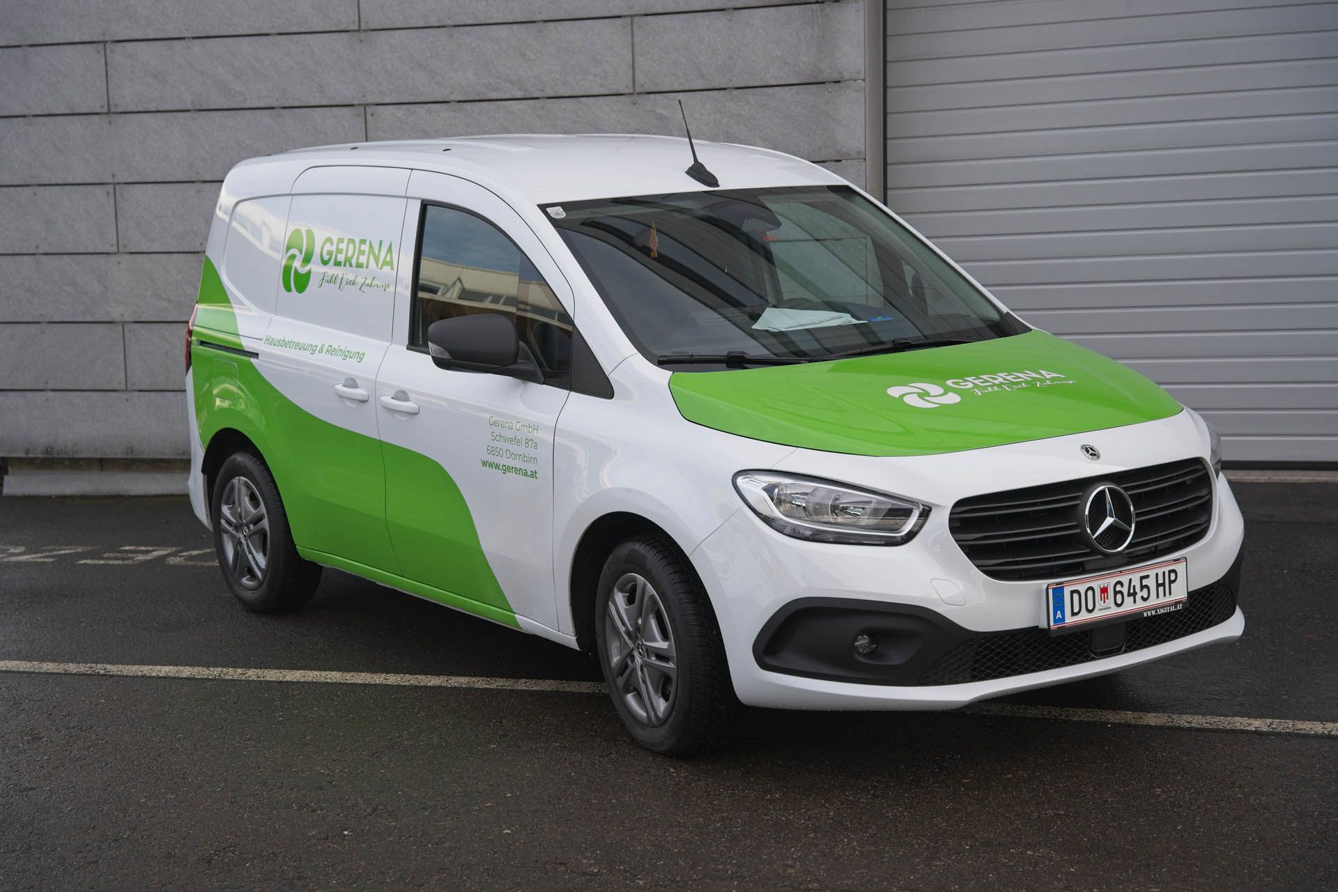 Ein weiß-grüner Mercedes-Transporter parkt vor einem grauen Gebäude.