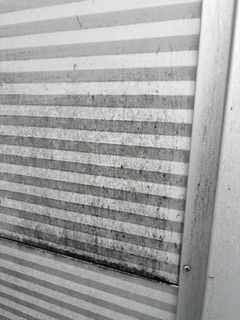 Eine Frau reinigt in der Küche einen Schrank mit einem grünen Tuch und einer Sprühflasche.