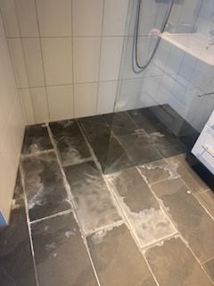 Eine Frau reinigt in der Küche einen Schrank mit einem grünen Tuch und einer Sprühflasche.