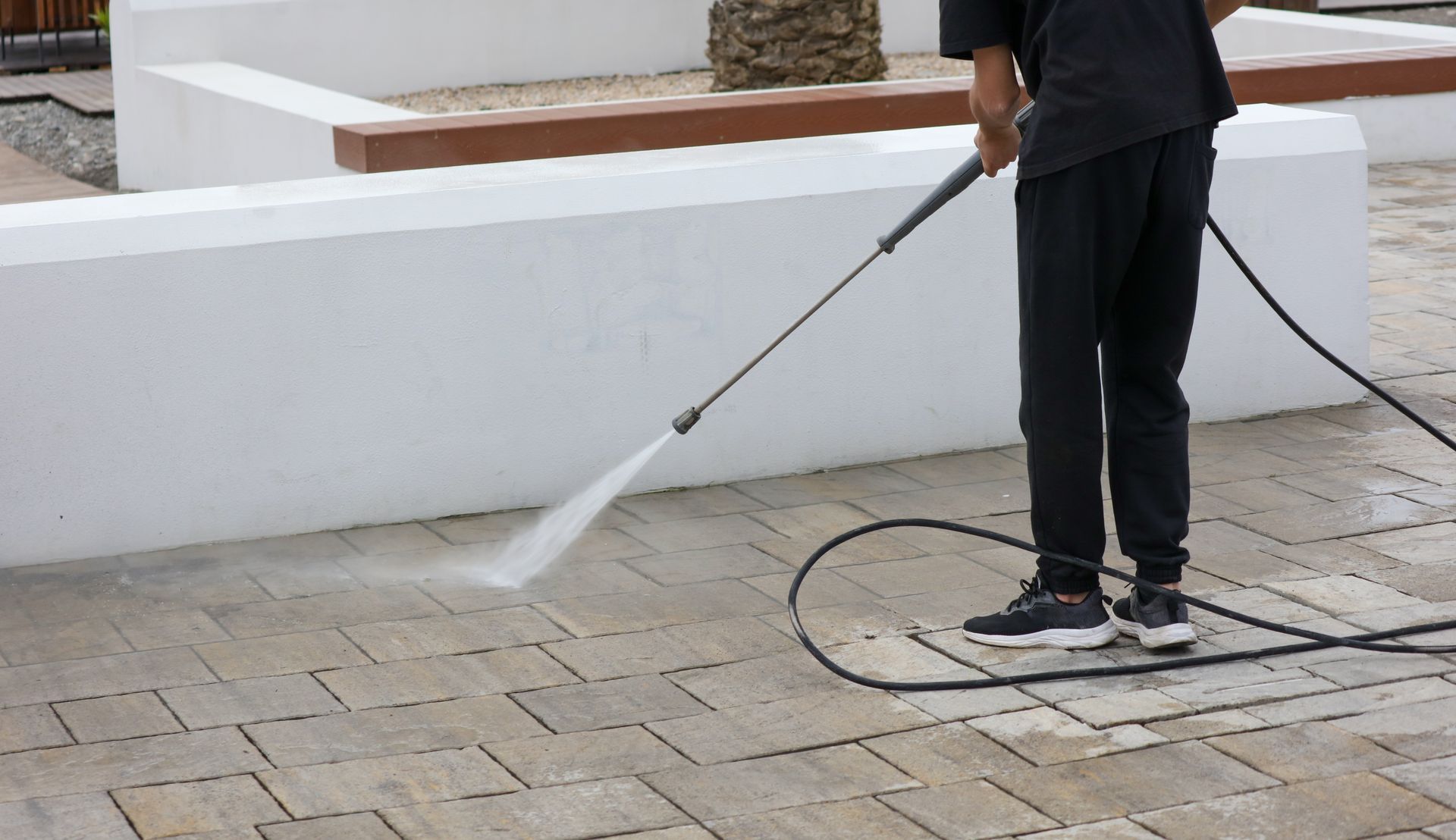 Eine Person reinigt eine Ziegelterrasse mit einem Hochdruckreiniger.
